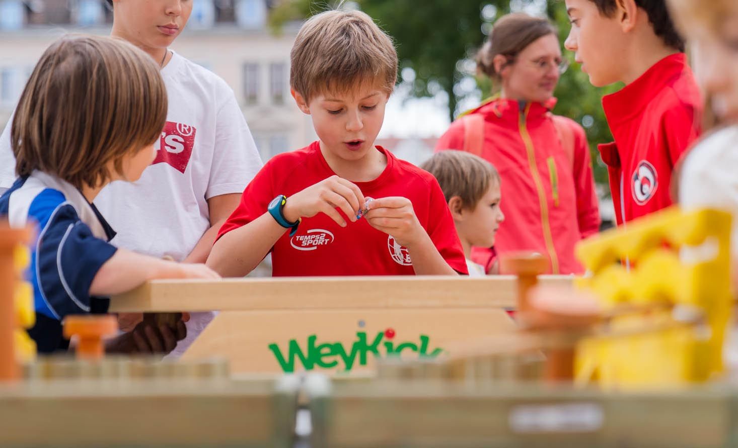 Trois enfants regardant un quatrième en train de faire une activité sur une table en plein air